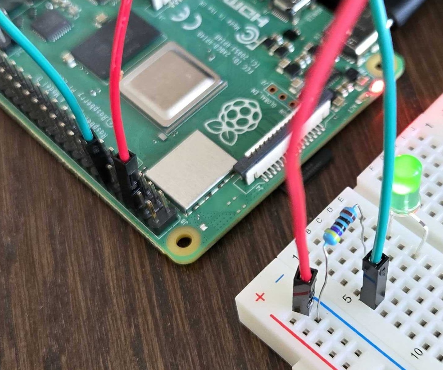 Image Alt Text:Raspberry Pi connected to a breadboard with a green LED and jumper wires alt-text