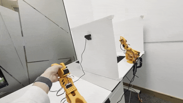 Image Alt Text:SO-101 teleoperation showing the operator moving the leader while the follower mirrors its arm and gripper motion across the workspace.